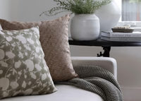 Decorative pillows and a blanket on a sofa with a small table in the background
