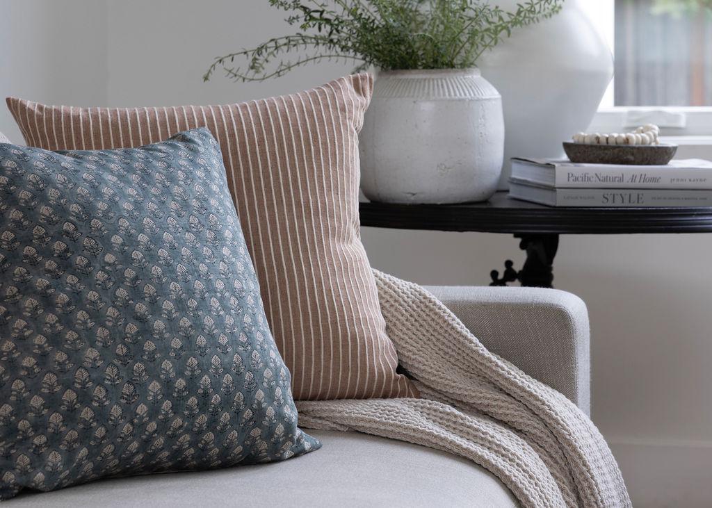 Decorative pillows and a blanket on a sofa with a small table in the background.