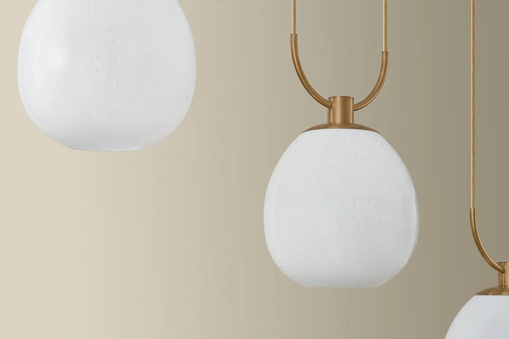 Close-up of a modern pendant light with white glass shades and gold metal fixtures against a beige background.