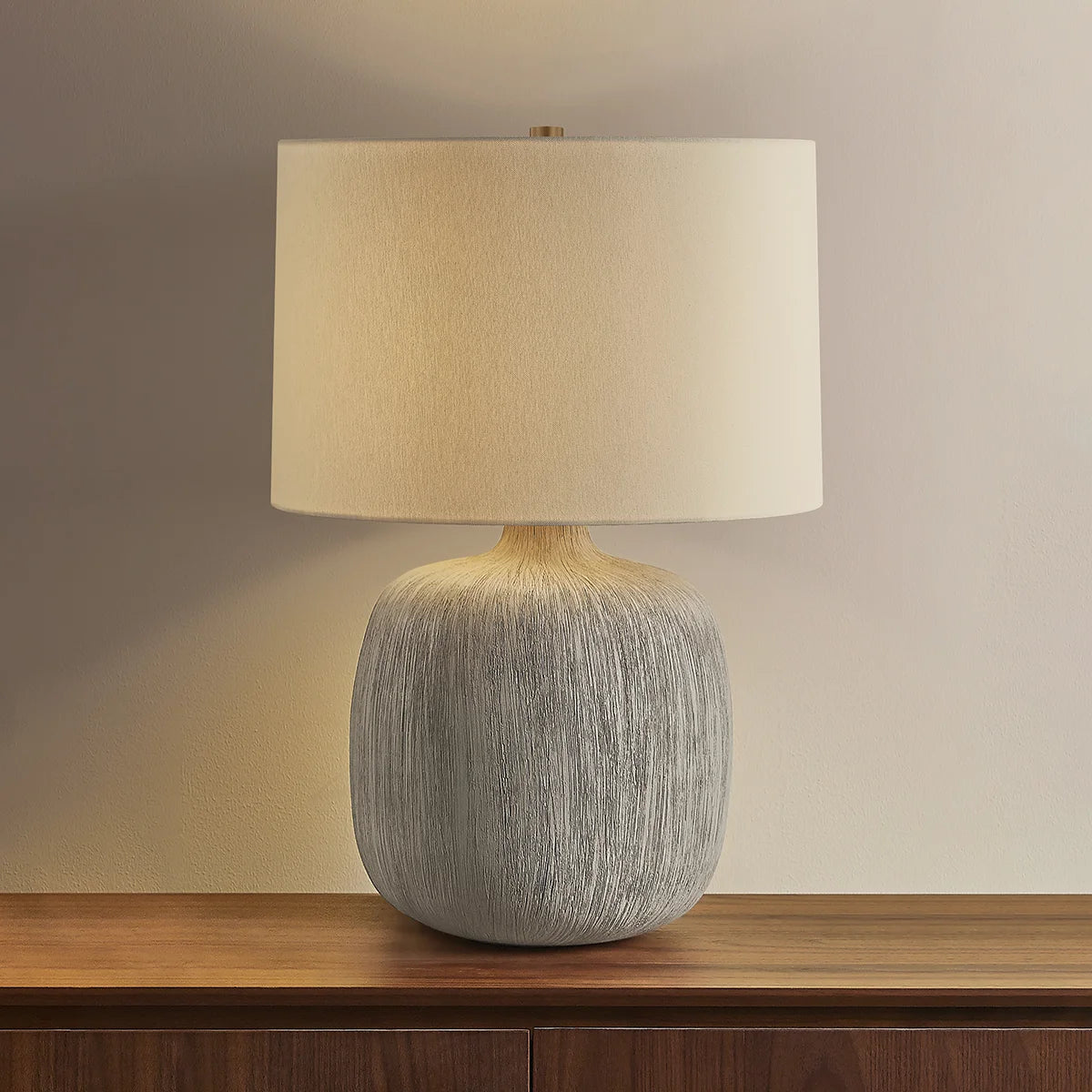 Table lamp with textured base and beige shade on a wooden surface.
