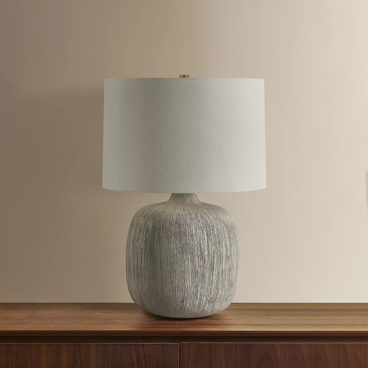 Table lamp with textured base and white shade on a wooden surface against a beige wall