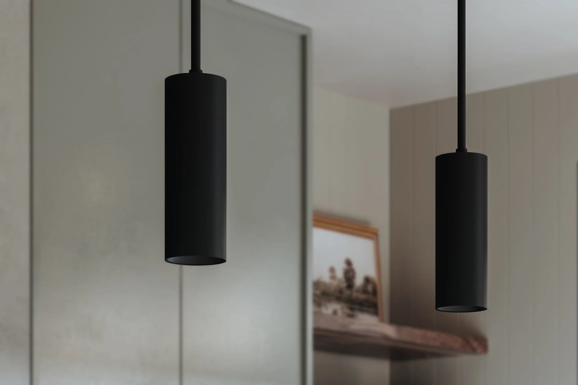 Modern black cylinder pendant lights hanging in a minimalist kitchen interior