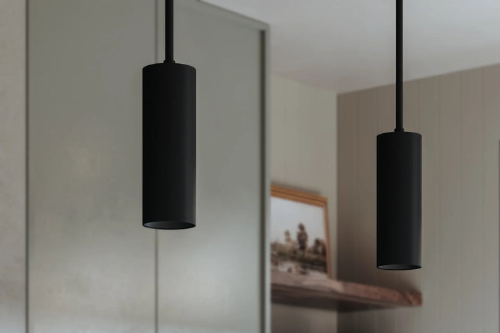 Modern black cylinder pendant lights hanging in a minimalist kitchen interior