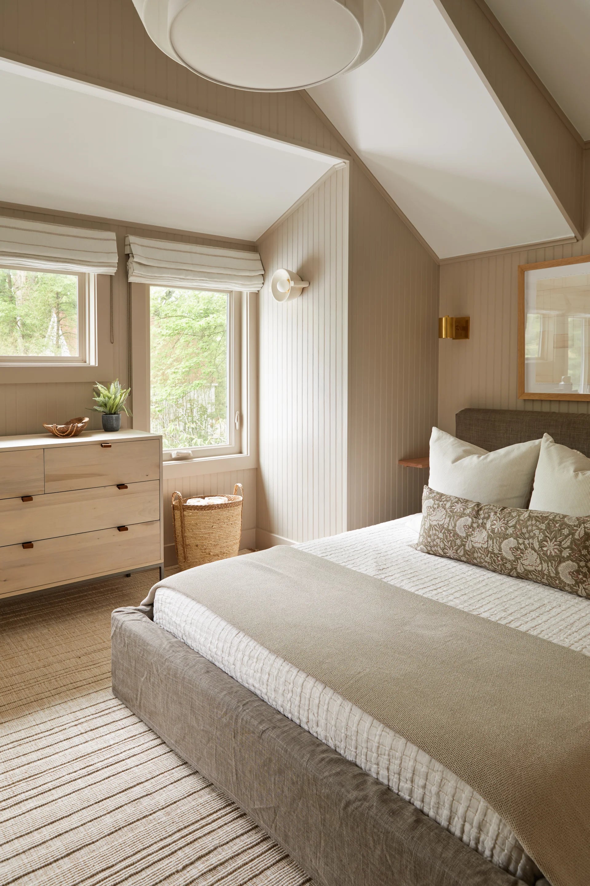Modern bedroom with a bed, dresser, and large windows.