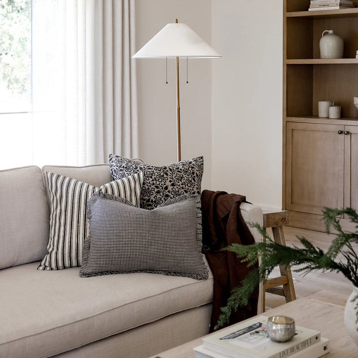 A modern living room showcasing a couch with a Myer Stripe Pillow Cover, a lamp beside it, and a bookshelf nearby.