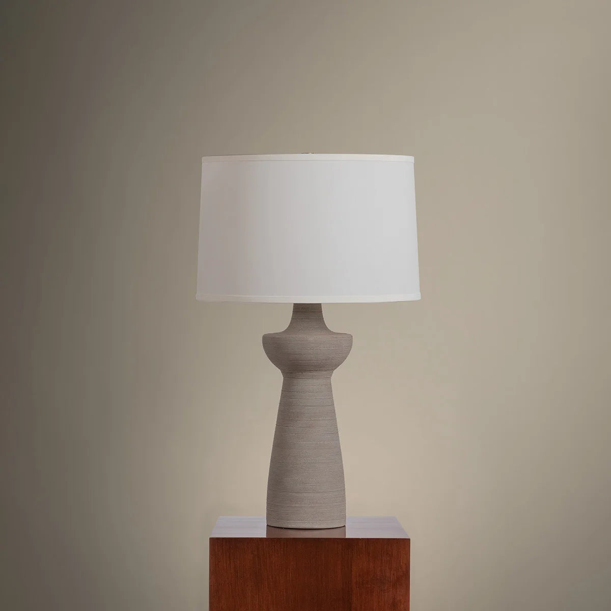 Table lamp with a white shade on a wooden pedestal against a beige wall
