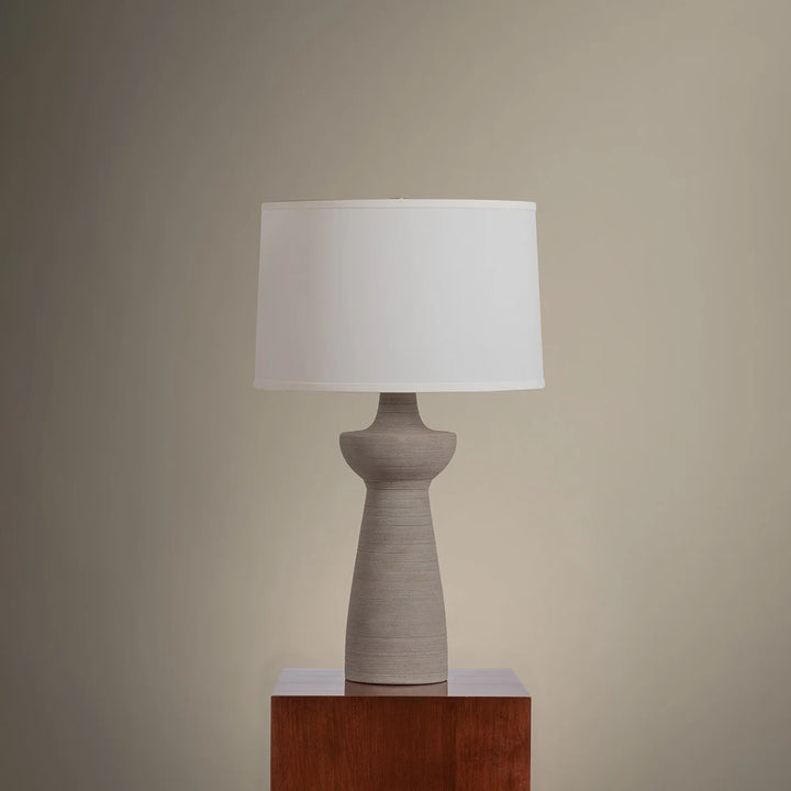 Table lamp with a white shade on a wooden pedestal against a beige wall