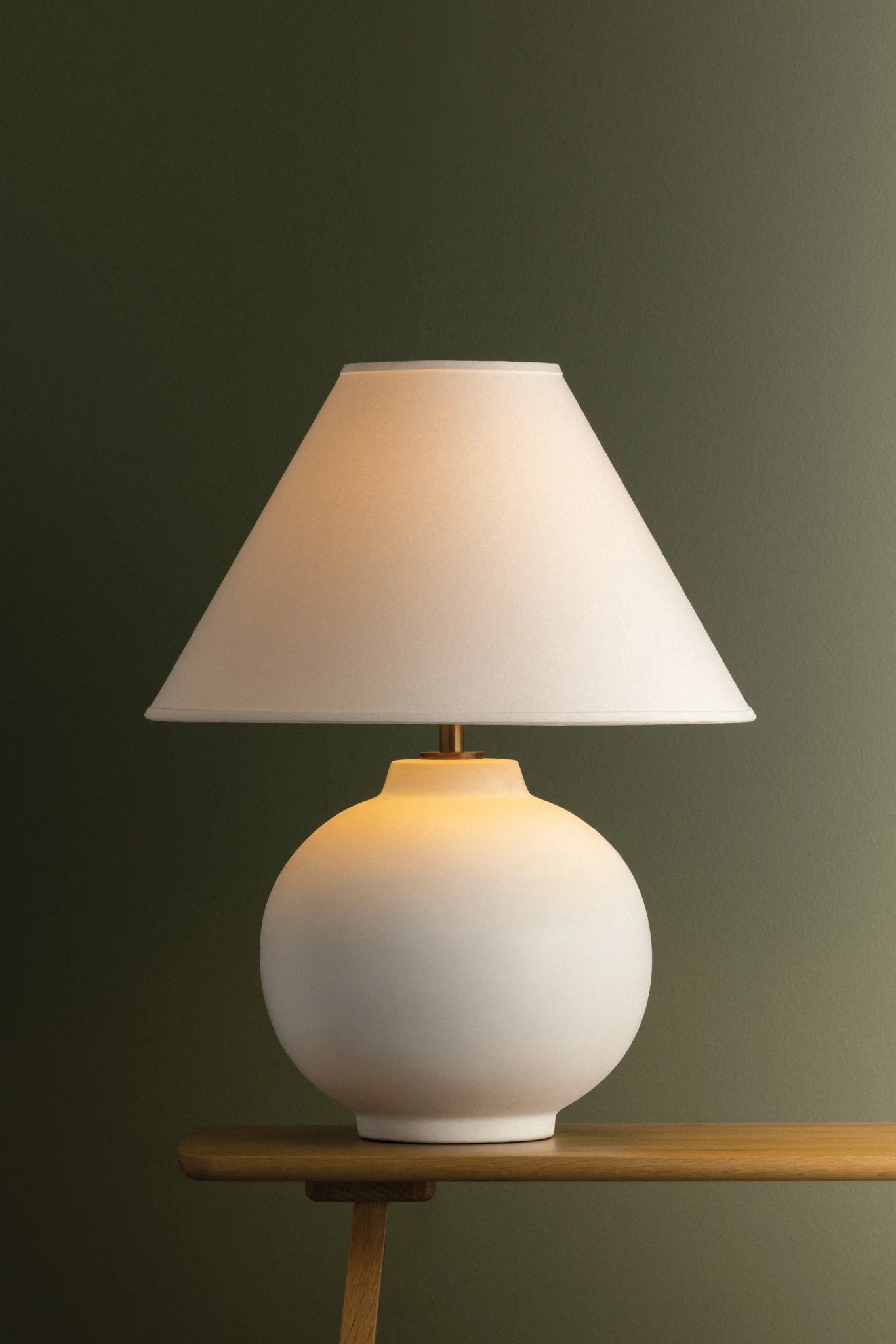 White table lamp with a beige shade on a wooden table against a dark green wall