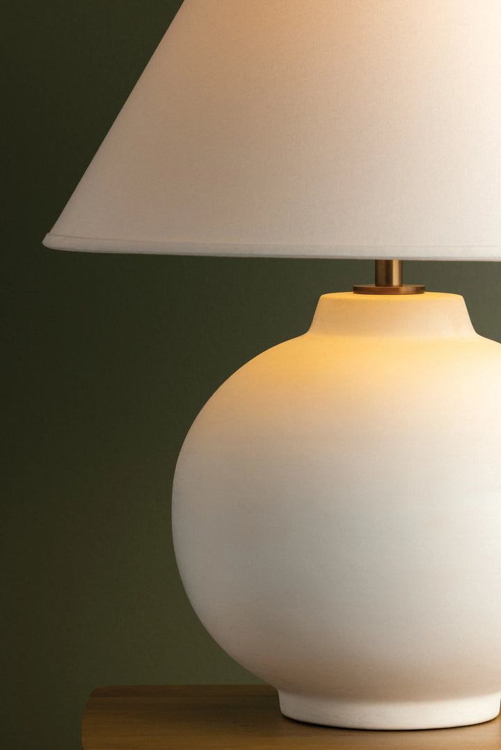 White table lamp with a beige shade on a wooden surface against a dark green background