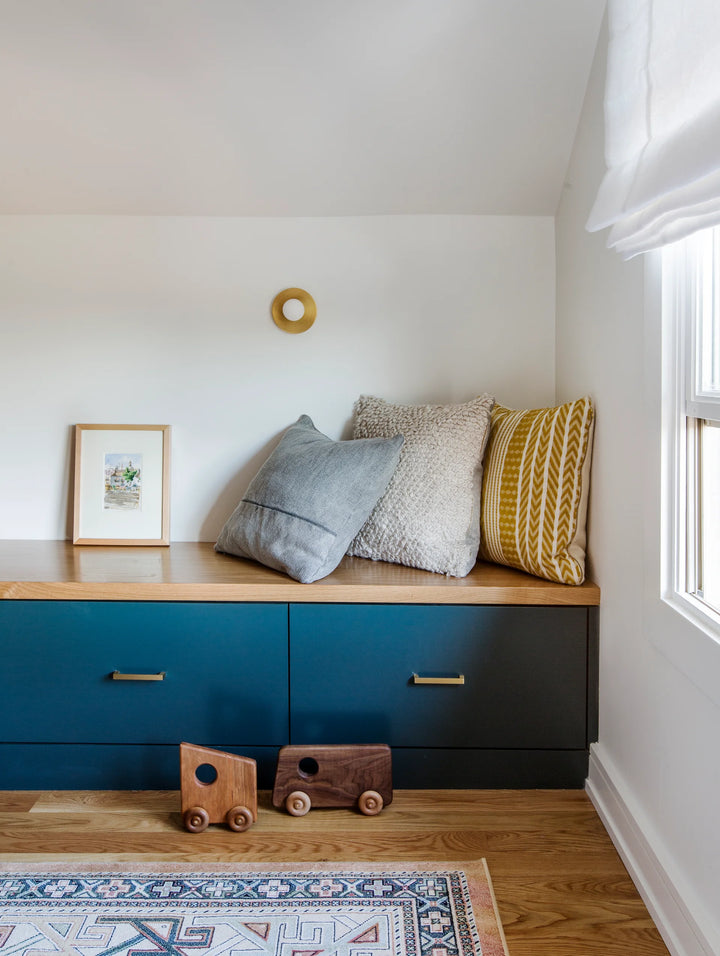 Nook with blue cabinets, wooden bench, and decorative pillows in a room with a window.